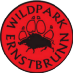 Schwarzer Kreis und Mitte rot gefüllt, der Schriftzug "Wildpark Ernstbrunn" füllt den Kreis als Kurventext und in der Mitte ist die Wolfspfote mit Wildschwein